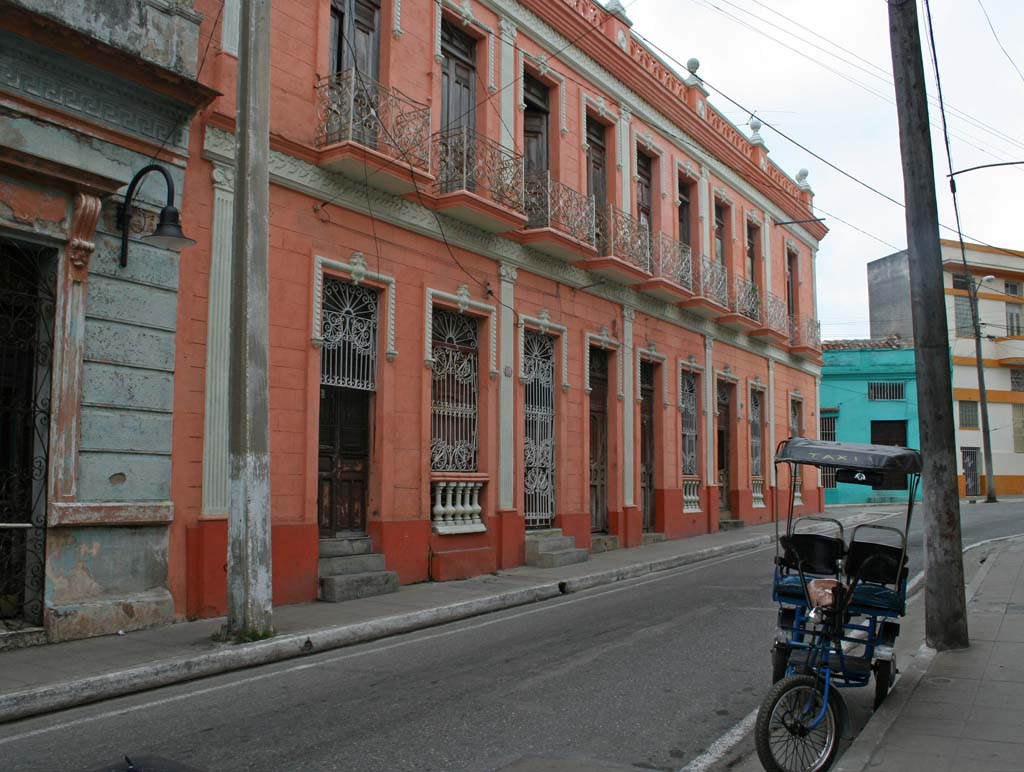 A bicitaxi parked opposite an elegant building.