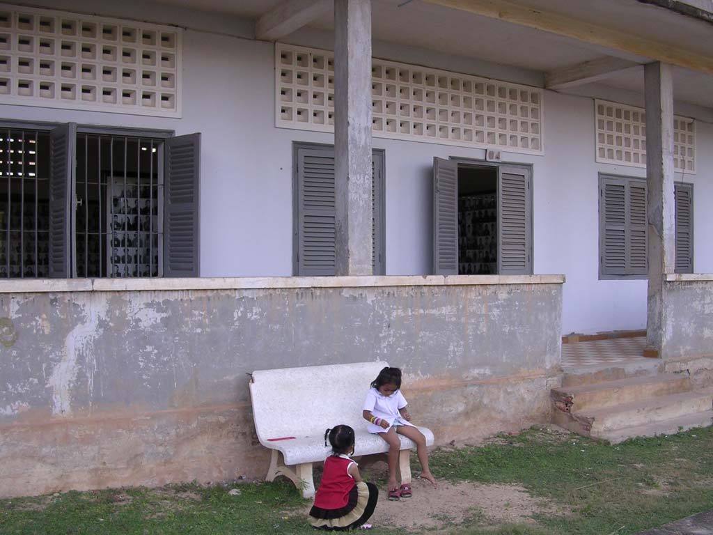 Two local girls play innocently, while photos of the victims are on display inside the building