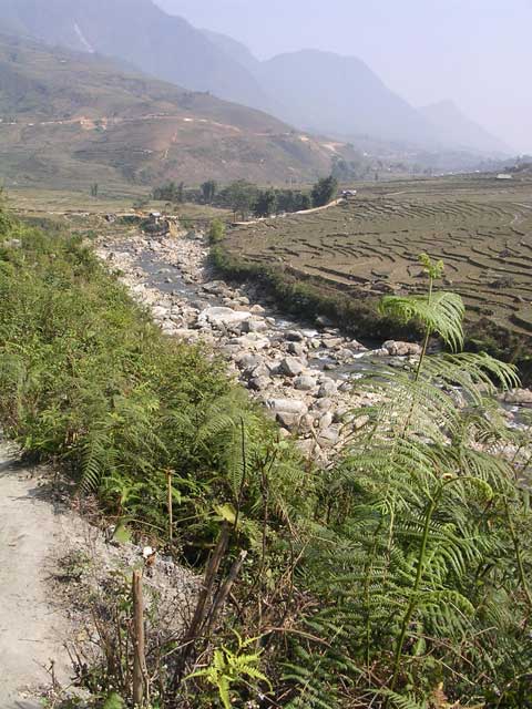 View of the river, with a bridge we're on our way to, paddies and the mountains beyond